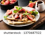 French crepes with strawberries and chocolate sauce on a plate served on wooden cutting board. Closeup view. Tasty sweet breakfast, lunch or dessert