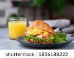 Delicious croissant sandwich with ham, cheese and scrambled eggs on plate served with glass of orange juice