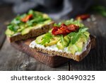 Healthy toast with goats cheese, avocado, arugula and sun dried tomatoes on rustic wooden table. Selective focus, close up