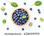 Fresh organic blueberries in wooden bowl, baby kiwi and baby spinach leaf on white background, top view. Flat lay or food pattern.