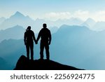 Silhouette Couple of man and woman reaching mountain top enjoying freedom and looking towards blue mountain silhouettes and sunrise. Alps, Allgaeu, Bavaria, Germany.