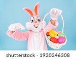 Easter bunny or rabbit or hare with basket of colored eggs, shows thumb finger up, having fun, dancing, celebrates Happy easter. Easter rabbit isolated on blue background