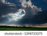 Small photo of Beautiful landscape with thundercloud and sunshine over a green field on a spring day.