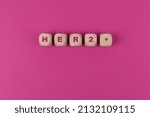 Small photo of HER2+ Breast Cancer Acronym, health support and hope concept. Wooden cubes isolated on Pink, copy space.