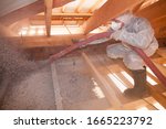 A man is spraying ecowool insulation in the attic of a house. Insulation of the attic or floor in the house