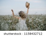 Pretty girl with a hat in her hand walks in a field with field flowers and smiles sincerely