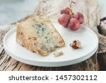 Small photo of A slice of blue aged Stilton cheese on a wooden table. Cheese is served with large grapes. Quality of agricultural products of farmers. Delicious English cheeses from Russian farmers