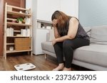 Small photo of Sad woman with fat upset bored of dieting Weight loss fail  Fat diet and scale sad asian woman on weight scale at home weight control.