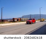 Small photo of Corinth, Peloponnese, Greece. July 2021: A road with cars and a railway with abandoned wagons against the backdrop of mountains in the city of Corinth in Greece
