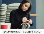 Small photo of Woman Make Notes And Look Around For Ideas. Portrait Of Stylish Smiling Woman In Winter Clothes Make Notes And Look Around For Ideas. Female Winter Style. - Image