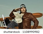 stock-photo-portrait-of-a-vintage-pilot-with-leather-cap-scarf-and-aviator-glasses-salutes-in-front-of-a-1108990982.jpg