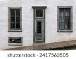 Small photo of The exterior of a vintage white masonry wall with multiple glass windows, half glass single door, transom window over the entrance and green colored trim. The facade of the house is on a steep hill.
