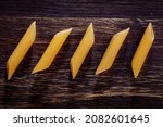 Small photo of Delicious looking pene pasta lying on a dark brown wooden table. Appetizing photo.