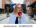 Small photo of Caucasian business blonde woman outdoors hold mobile phone read unpleasant sms awful news feel indignant. Bad notice from bank blocked account broken smartphone shock astonishment