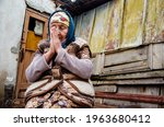 Small photo of Ask for help. Poverty and misery. Slums. Poor areas. Seniors concept. The old grandmother bowed her head in prayer.The old grandmother on the background of the slums. Grandma is praying.