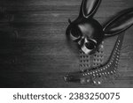 Small photo of Black rabbit mask, studded leather bracelets and neck choker on the black wooden table background with copy space.