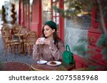 Small photo of romantic sophisticated woman drinking coffee or cappuccino in a french cafe on street. romantic sophisticated girl sits at a table in pastry shop or bakery