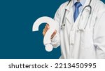 Small photo of Midsection of a doctor in uniform holding a white question mark while standing on a blue background. Space for text. Healthcare concept