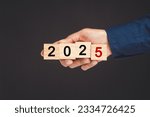 Close-up of hand holding wooden cubes with the letters 2025 against a black background. Countdown and Business Planning to 2025.