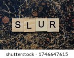 Small photo of gray word slur from wooden letters in black font on a brown shabby wall with a pattern