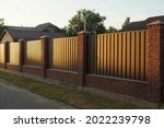 part of a long wall of a fence made of brown bricks and metal outside in the evening