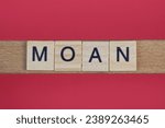 Small photo of text the word moan from gray wooden small letters with black font on an red table
