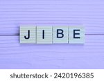 Small photo of word jibe from small gray wooden letters lies on a pink wooden table