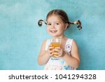 Small photo of Smiling girl with funny pigtails like Pippi keeps glass of fresh orange juice