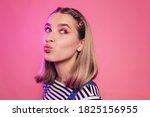 Small photo of Positive amazing young caucasian woman blowing a kiss to someone and looking away. Isolated over pink background. Lips in a tubule. Bright makeup, smart casual style concept