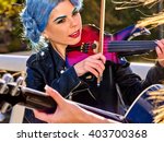 Music street performers girl with blue hair violinist  playing  aganist sky with clouds outdoor. The second girl - violinist with her.