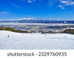 The Tokachidake Mountain Range seen from Furano Ski Resort on a sunny day, skiers skiing the vast beginner course in the Kitanomine Zone
