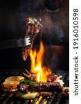 Small photo of Grilled pork ribs on the grill chopped on a fork against a fire. The cook holds a fork in his hand. concept cooking meat. Close up. place for text.