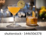 A sweet and sour citrus drink with a lemon wedge stands next to a whiskey at the bar of an an upscale, expensive restaurant.