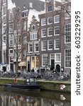 Small photo of Amsterdam, The Netherlands - 18 February 2014: Canal houses along Singel canal with art deco ironmonger store sign, pedestrians, parked bicycles, and moored boat
