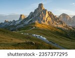 Sunrise at Passo Giau with road and parked cars and campers with sun shining at meadow and peaks in  the background during summer morning in august
