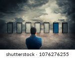 Rear view of a businessman in front of many doors choosing the one different colored. Difficult decision, concept of the important choice in life, failure or success. The ways to unknown future, busin