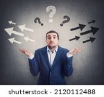 Small photo of Perplexed businessman shrugs shoulders, hands outstretched, has doubts to choose left or right side. Puzzled male express uncertainty, has questions as different arrow points opposite directions