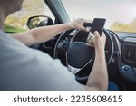 Young driver guy distracted by his phone while in front of the steering wheel, using his smartphone with one hand while driving. Risk and danger situations on the road, violating traffic rules