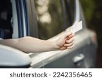 Small photo of Close up person hand out of the car window holding the driver license as shows it to the police officer for control