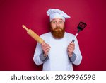Small photo of doubter chef with beard and red apron chef holds wooden rolling pin