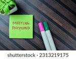 Small photo of Concept of Meeting Postponed write on sticky notes isolated on Wooden Table.