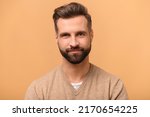 Handsome charismatic bearded man looking at the camera, close-up portrait, studio shot isolated on beige