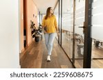 Businesswoman carrying laptop walking through hallway going to leave office after workday, full lengths portrait of cheerful confident freelance woman walking in modern coworking space