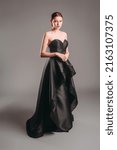 Small photo of Black ball gown. Attractive ginger young woman in sleeveless evening dress on studio background. Holiday outfit. A line timeless dress with sweetheart neckline. Dramatic portrait.