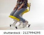 Small photo of Woman is sitting on kneeling chair in office isolated on white. Ergonomic chair with wheels. Therapeutic stool with back support. Orthopaedic stool for desk based distance work from home.