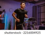 Small photo of Handsome young asian man exercising, having workout on a treadmill in living room. Happy male running, having cardio training at evening, night time at home, healthy lifestyle concept.