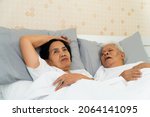 Small photo of Older Asian woman laying open her eyes in bed beside her husband who snores and Makes noise, Marital problems.