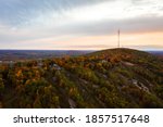 Beautiful aerial drone photograph of rib mountain with colorful fall leaves or autumn foliage lining the grassy ski runs at sunset as the cloudy sky turns orange and pink above the horizon.