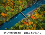 Beautiful travel or tourism style look down aerial of pedestrian foot bridge across the Bad River at Copper Falls park with colorful fall foliage lining the river banks in autumn in Mellen, Wisconsin.