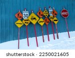 Series of colourful speed, road work, stop, slow, truck crossing and other signs set in snow against blue metal-clad wall, Saint-Augustin-de-Desmaures, Quebec, Canada